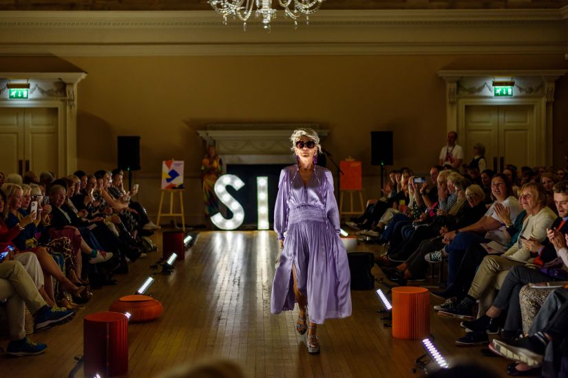 Woman walking down fashion runway wearing purple dress