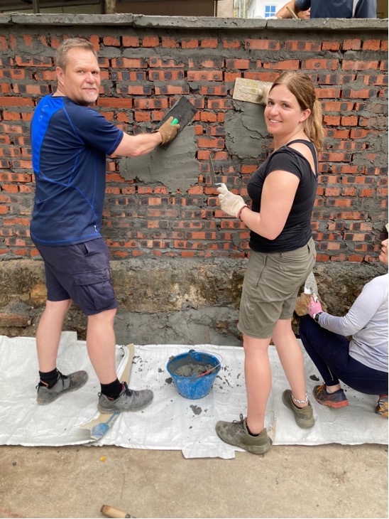 Man and woman from hospice trekking team building a brick wall