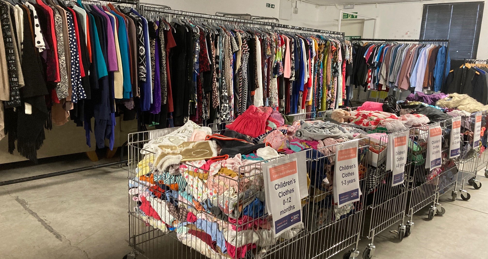 Full rails of clothing at the Warehouse, with full metal baskets of children's clothing in front